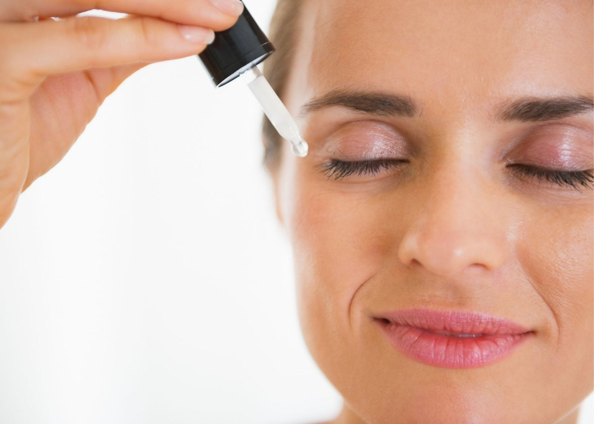 Woman with eyes closed applying botanical oil with a dropper