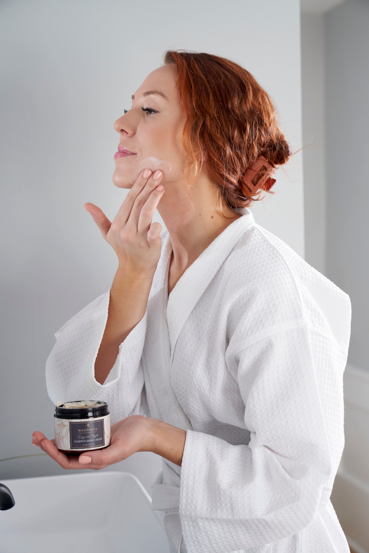 Woman in a white robe applying cream from a jar