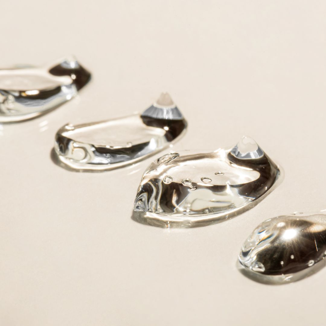 Clear hyaluronic acid gel droplets on a beige surface