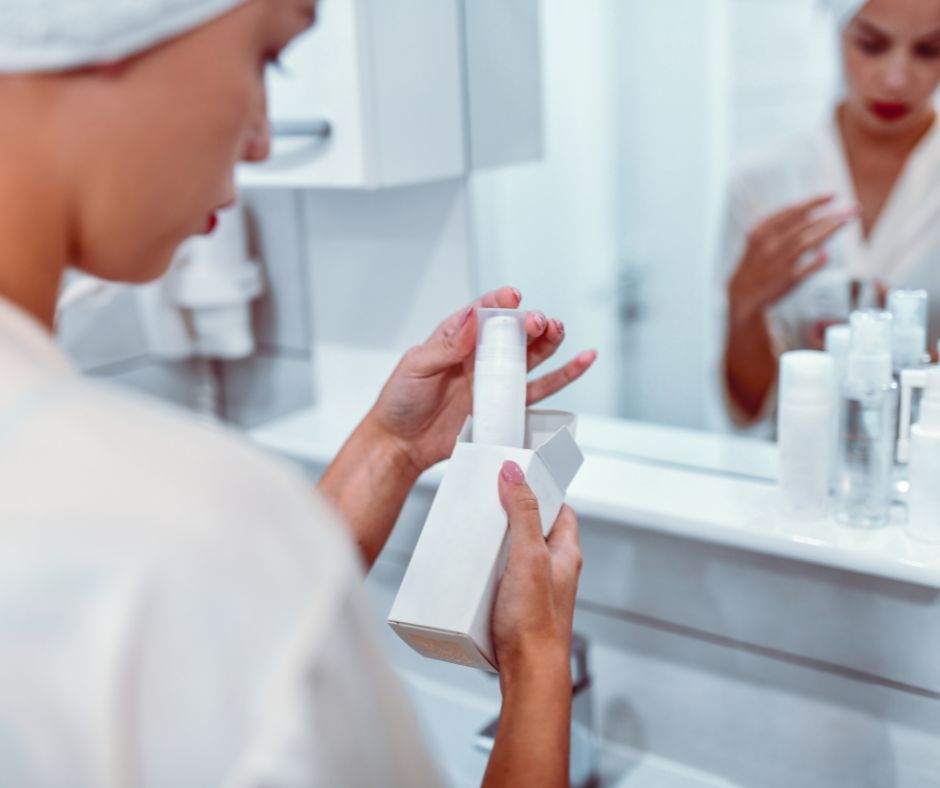 Woman in a towel wrap reading a skincare product label at the sink