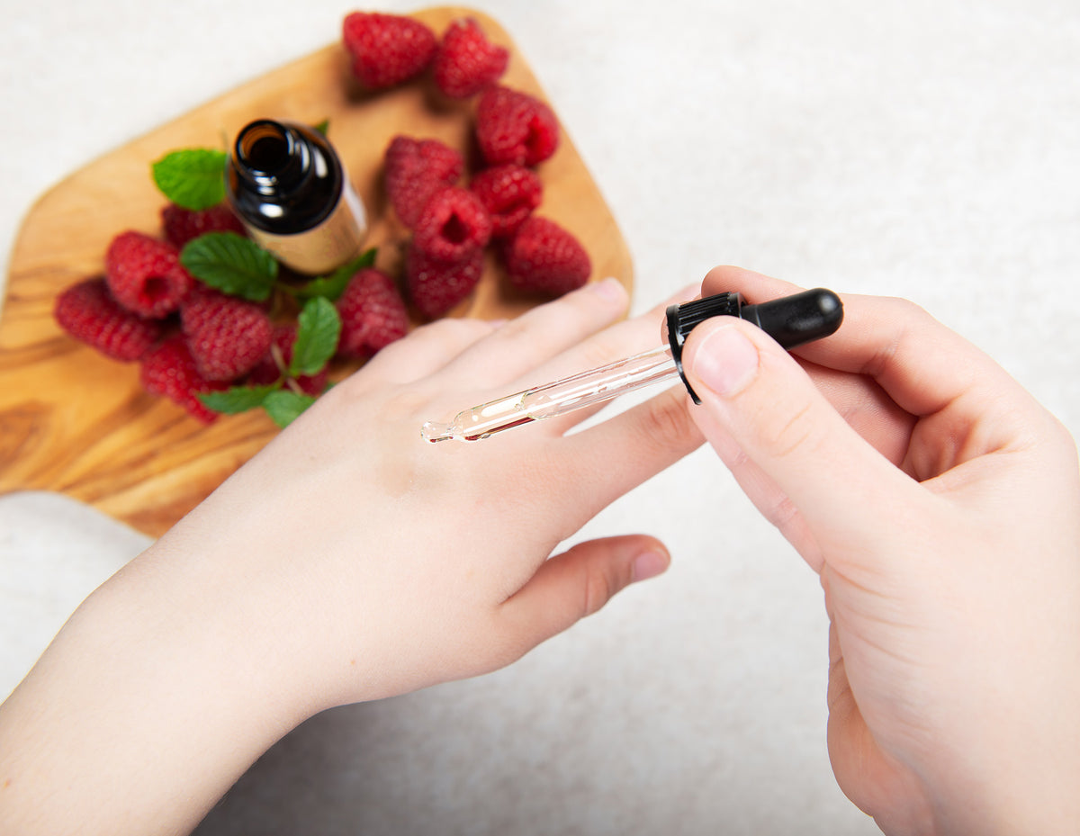 Raspberries and a dropper of botanical oil on a hand