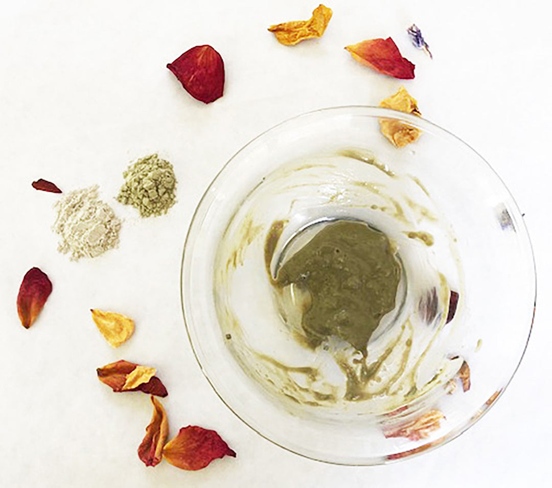 Clay mask in a glass bowl with dried rose petals and botanical powders