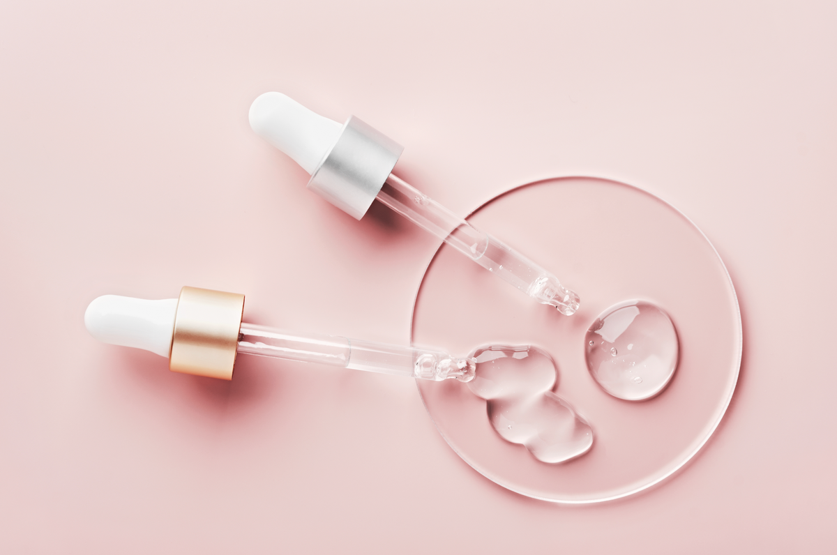 Two droppers with clear serum drops on a pink background