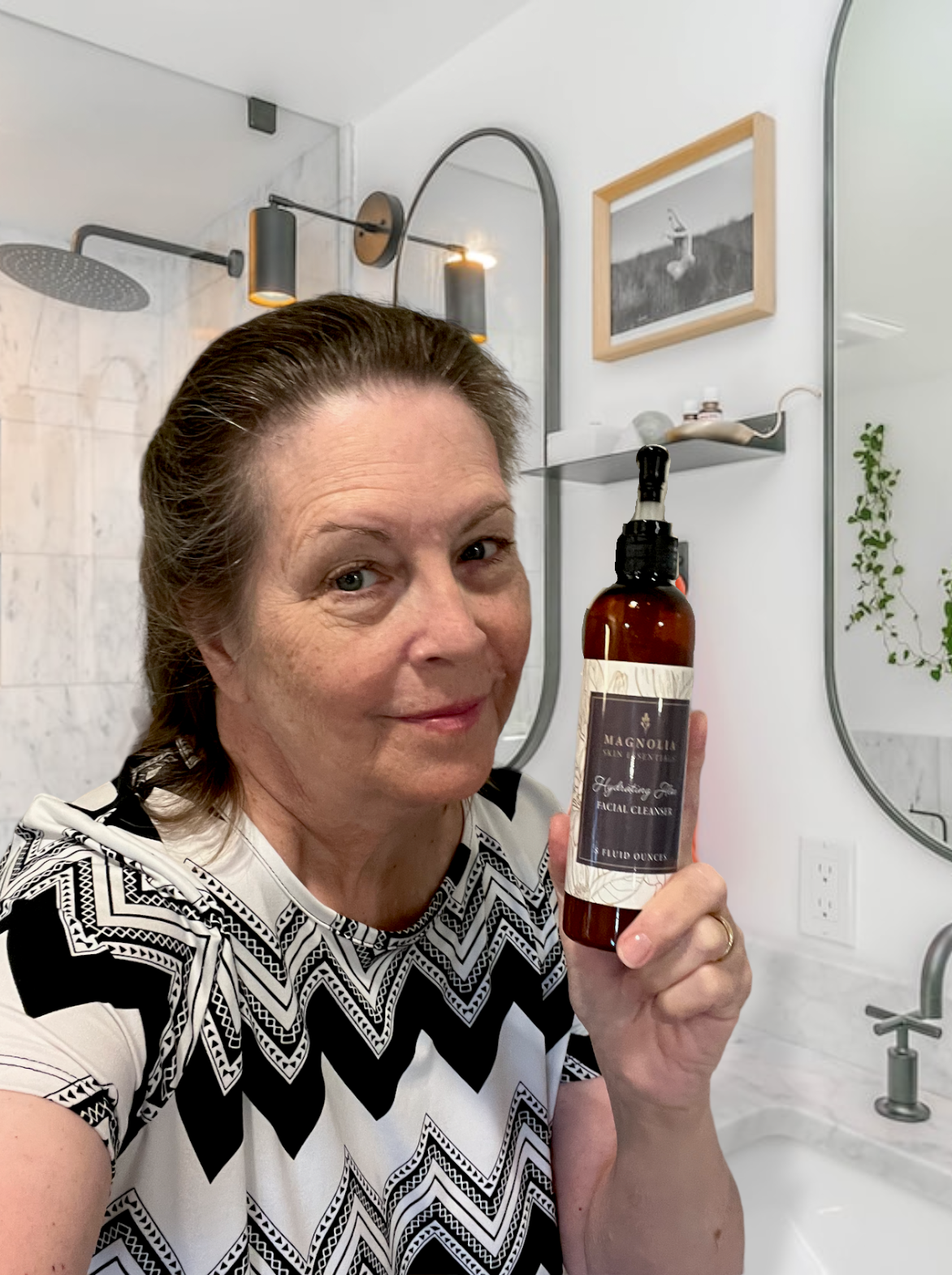 Smiling woman holding a Magnolia Skin Essentials pump bottle in her bathroom