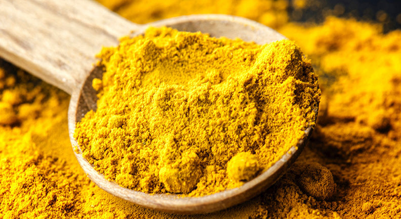 Wooden spoon filled with bright golden turmeric powder