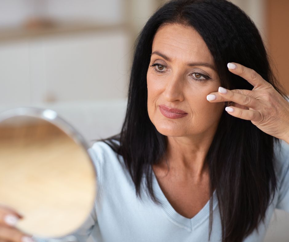 Dark-haired woman checking her skin in a hand mirror