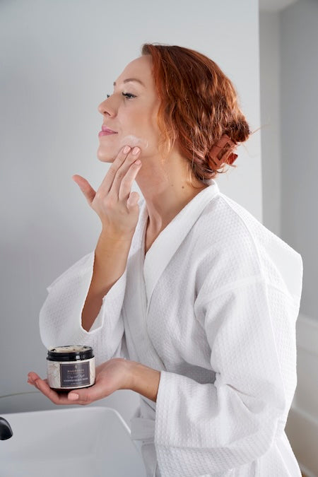 Woman in a white robe applying Magnolia Silk Hydraluxe Crème to her face