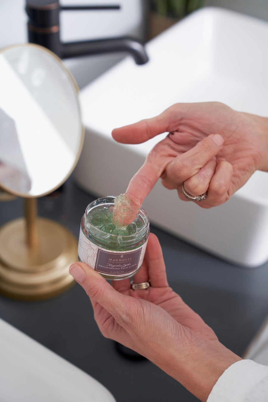 Fingertip scooping Magnolia Jojoba Brightening Face Scrub from the jar