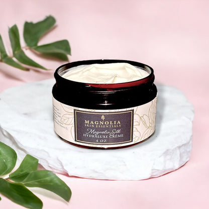 Magnolia Silk Hydraluxe Crème jar on marble with green leaves